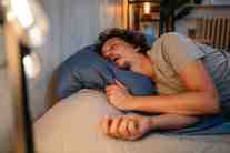 A man sleeping on his side at home while snoring loudly due to undiagnosed sleep apnea.